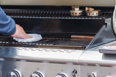 Person reinigt Gasgrill mit Tuch.